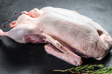 Raw whole duck, pink pepper and rosemary. Black background. Top view