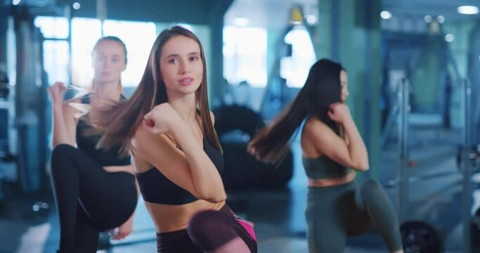 Active multi-race group of three amazing fitness women performing intense exercises warm-up bodycare workout in professional gym environment. Team sports,