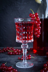 Red currant drink in a glass goblet on a gray cement surface. A bunch of red currants on a glass