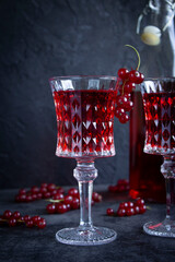 Beautiful glass goblet with red currant alcohol drink, bunch of currants on a glass. Bottle with red drink