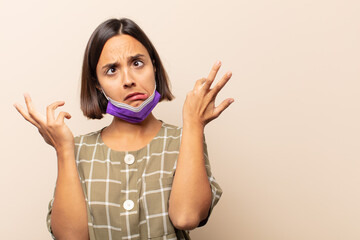 young hispanic woman shrugging with a dumb, crazy, confused, puzzled expression, feeling annoyed...