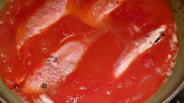 Scenes of life at home: cooking the mullets in sauce, tilt movement on the pan where the mullets are immersed in the hot red sauce.