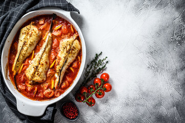 Cooking in tomatoes monkfish fish in a baking dish. Fresh seafood. Gray background. Top view. Copy...
