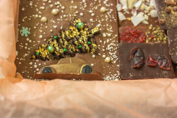 Handmade milk and dark chocolate bars in orange kraft paper, image of a car with a Christmas tree on the roof. No people
