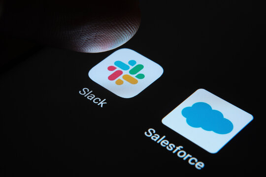 Stone, Staffordshire / United Kingdom - November 26 2020: Slack and Salesforce apps on the smartphone screen and a finger tip above one of them. Concept photo for merger deal. SELECTIVE FOCUS.