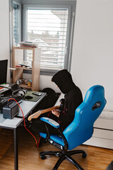 Young teenager boy in black hoodie playing electric guitar using amplifier in his room at home. Practicing music lesson online.