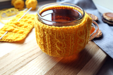 A cup of tea in a knitted yellow outfit with needlework, close - up-the concept of needlework classes in the winter season