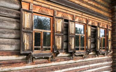 Windows with shutters of an old wooden house built of logs. Three windows on the facade of the village house in warm golden brown tones.