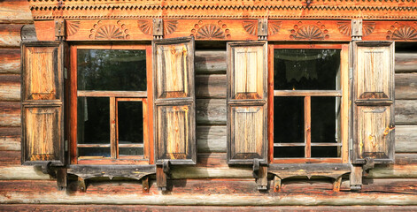 Windows with shutters of an old wooden house built of logs. two windows on the facade of the village house in warm golden brown tones