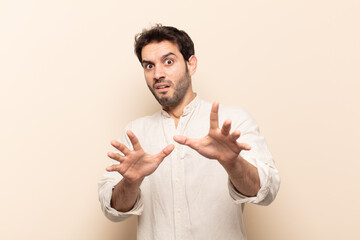 young handsome man feeling terrified, backing off and screaming in horror and panic, reacting to a...