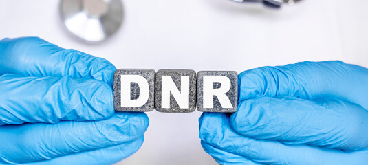 DNR Do not resuscitate - word from stone blocks with letters holding by a doctor's hands in medical protective gloves