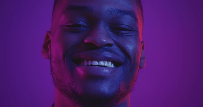 Close up portrait of happy african american guy laughing at camera in neon lights, slow motion
