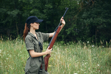 Woman on nature with a gun in his hands black cap green jumpsuit shooting fresh air 
