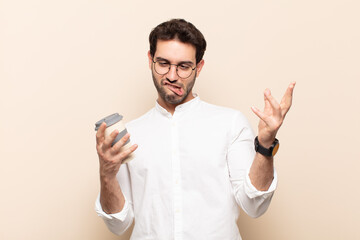 young handsome man shrugging with a dumb, crazy, confused, puzzled expression, feeling annoyed and...