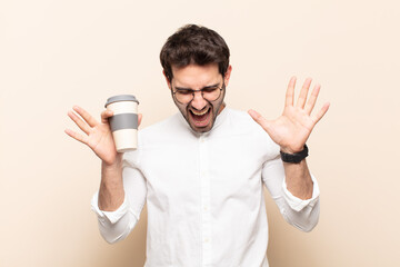 young handsome man screaming in panic or anger, shocked, terrified or furious, with hands next to...