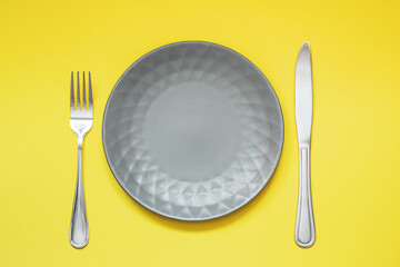 Empty gray plate and cutlery on yellow background. Trending Color of year - Illuminating and...