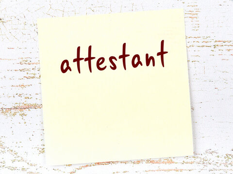 Yellow sticky note on wooden wall with handwritten word attestant