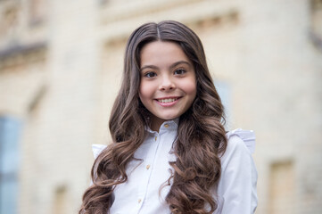 Fototapeta premium Happy beautiful kid with cute look wear long wavy hair outdoors, beauty