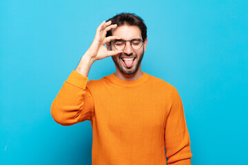 young handsome man smiling happily with funny face, joking and looking through peephole, spying on...