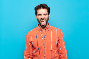 young handsome man feeling disgusted and irritated, sticking tongue out, disliking something nasty...