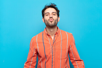 young handsome man pressing lips together with a cute, fun, happy, lovely expression, sending a kiss