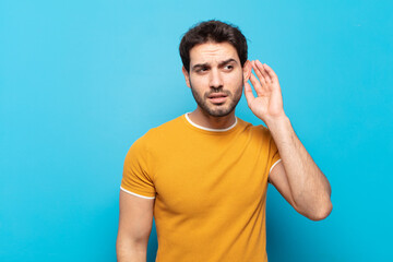 young handsome man looking serious and curious, listening, trying to hear a secret conversation or...