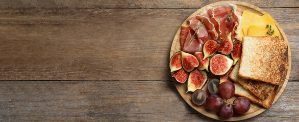 Delicious ripe figs, prosciutto and cheese served on wooden table, top view. Space for text