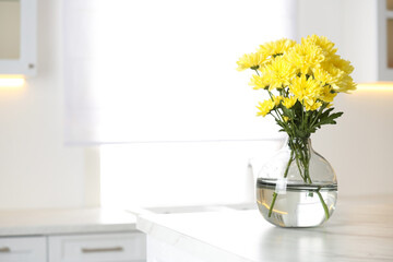 Vase with beautiful yellow chrysanthemum flowers on table in kitchen, space for text. Stylish element of interior design