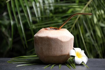 Obraz na płótnie Canvas Young peeled coconut with straw and flower on black table