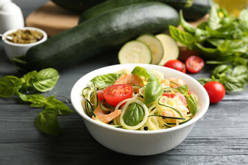 Delicious zucchini pasta with shrimps, cherry tomatoes and basil on grey wooden table