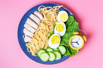 Plate with food on pink background and alarm clock, interval fasting concept