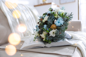 Beautiful wedding winter bouquet and book on sofa indoors, space for text. Bokeh effect