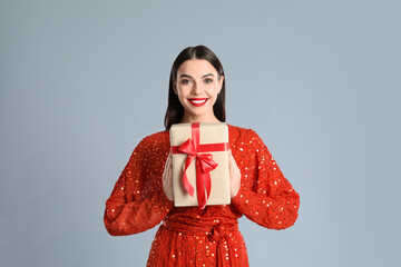 Woman in red dress holding Christmas gift on grey background