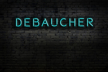 Neon sign. Word debaucher against brick wall. Night view