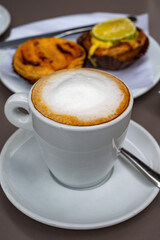 Cup of cappuccino coffee served with traditional dessert pastry in Portugal, nata eggs cream cakes with fruits
