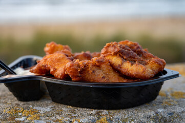 Dutch street seafood, deep fried cod fish fillet with garlic sauce called in Netherlands kibbeling and North sea beach on background