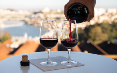 Pouring of fortified dessert ruby, tawny port wines in glasses with view on Douro river, porto lodges of Vila Nova de Gaia and city of Porto, Portugal