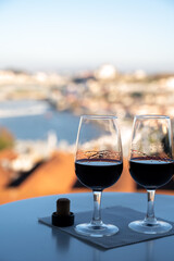 Tasting of different fortified dessert ruby, tawny port wines in glasses with view on Douro river, porto lodges of Vila Nova de Gaia and city of Porto, Portugal