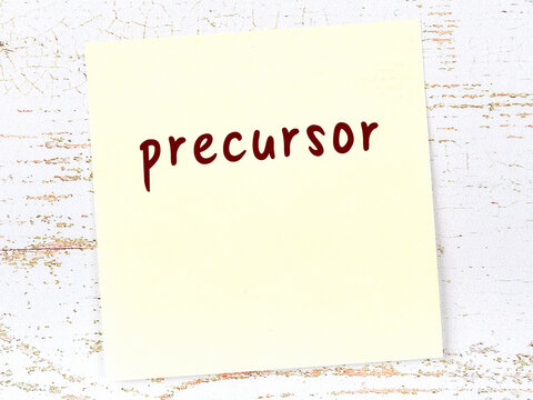Yellow sticky note on wooden wall with handwritten word precursor