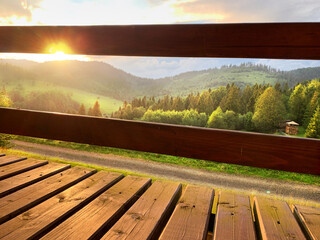 Fototapeta na wymiar Mountains and green hills landscape at sunset time. Vew from wooden terrace, balcony. Nature Outdoors Travel background