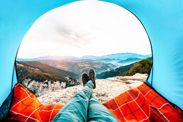 Man lying in a tent with the view of mountains and sunset - Sport, travel and lifestyle concept.