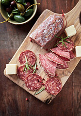 Sliced salami with fresh rosemary and olives on rustic wooden background. Top view. 