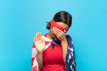 young latin woman covering face with hand and putting other hand up front to stop camera, refusing...
