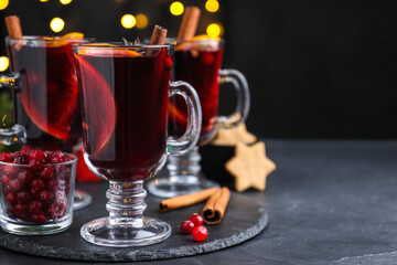 Aromatic mulled wine on black table against blurred festive lights, space for text