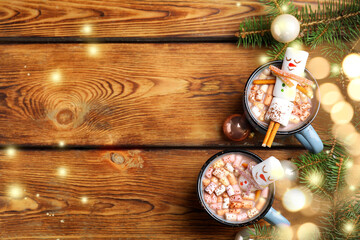 Flat lay composition with marshmallow snowmen in cups of hot drinks on wooden table, space for text. Bokeh effect