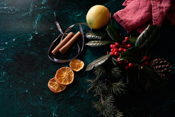 Arrangement of Christmas decorations: green conifer, red berries, ribbons and oranges on a dark background. 