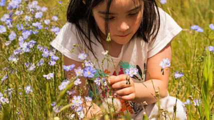 children playing and smelling blue flowers on a sunny day in a grass field
