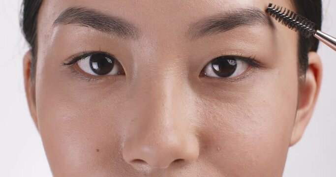 Eyebrow lamination and styling. Close up shot of young asian woman combing her eyebrows, looking at camera