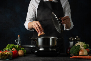 Professional chef pours chicken fillet into pan for cooking soup on dark blue background. Backstage of preparing meal. Healthy dish. Food concept. Frozen motion. Cookbook.