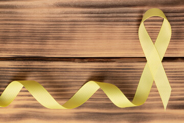 Yellow awareness ribbon on wooden background. Sarcoma. Childhood cancer. World Cancer Day. Flat lay. Copy space